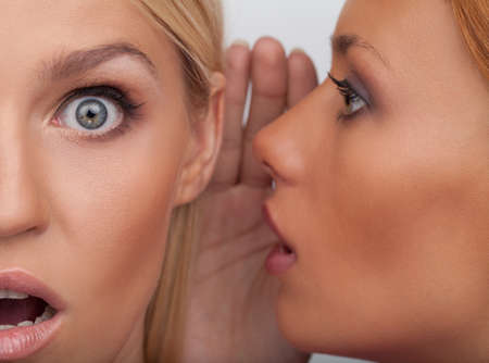 It is unbelievable! Close-up of two beautiful young women gossiping while standing isolated on whiteの写真素材