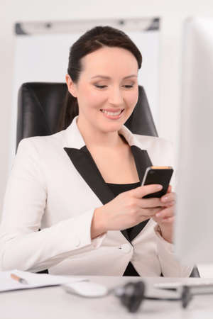 Dialing a number. Beautiful middle-aged businesswoman sitting at her working place and dialing number on the mobile phoneの写真素材