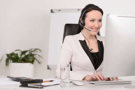 Customer service representative at work. Beautiful middle-aged customer service representative typing something on computer and smilingの写真素材