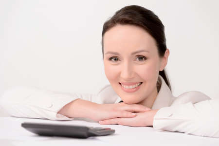 Smart and beautiful. Portrait of beautiful middle-aged businesswoman leaning on the table and smiling with a calculator on the foregroundの写真素材