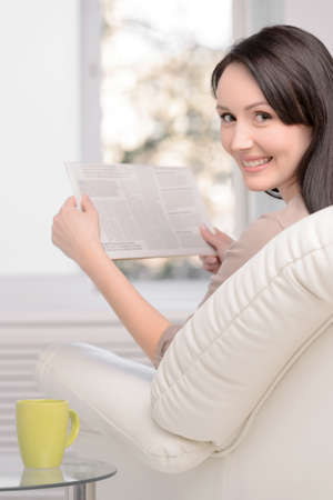 Only good news. Beautiful middle-aged woman sitting on the couch reading a Sunday paperの写真素材