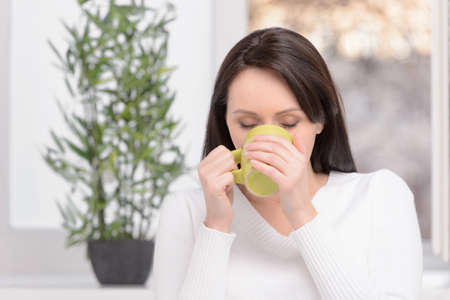 Enjoying her coffee. Beautiful middle-aged woman standing in front of the window drinking coffeeの写真素材