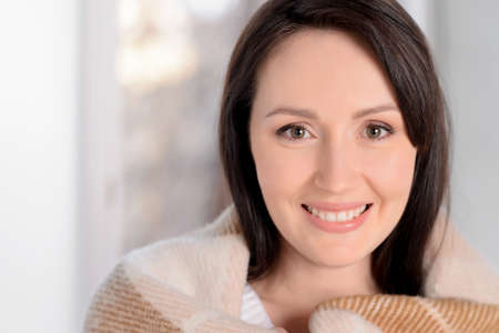 So warm and cosy. Portrait of beautiful middle-aged woman covered with plaid smiling at cameraの写真素材