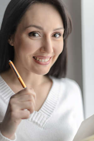 Birth of new idea. Beautiful middle-aged woman holding a oen in her hand and looking at cameraの写真素材