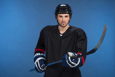 Handsome hockey player standing isolated on blue background. Holding hockey-stickの写真素材