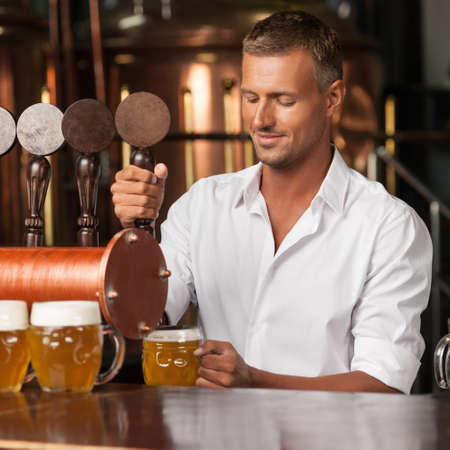 Serving the best beer in town. Handsome bartender in white shirt serving beerの写真素材