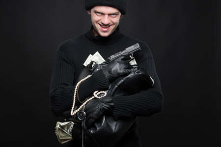 Burglar with stolen goods. Angry burglar holding stolen goods while smiling against black backgroundの写真素材