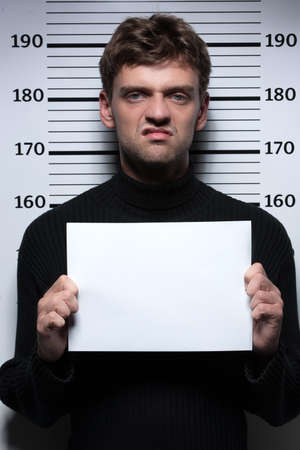 Busted burglar. Angry burglar holding a white poster while standing against police line-upの写真素材