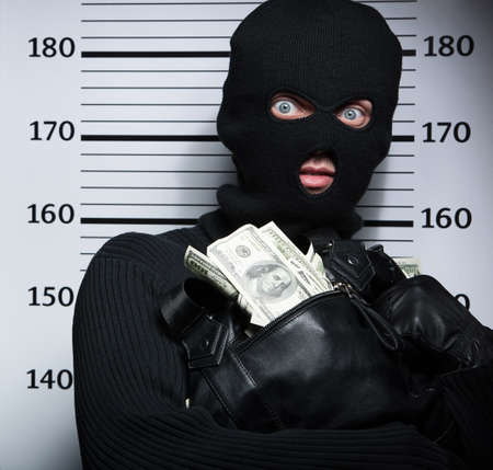 Busted burglar. Angry burglar holding a bag with stolen goods while standing against police line-upの写真素材