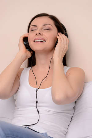 Listening to her favourite music. Beautiful middle-aged women sitting on couch and listening to the music with her eyes closedの写真素材