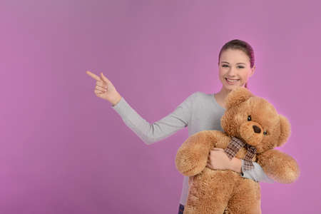 Teenage girl pointing. Happy teenage girl holding a teddy bear and pointing away while isolated on coloured backgroundの写真素材