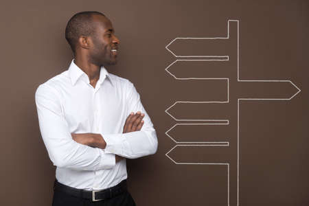 Young businessman looking at many arrows on the brown wall