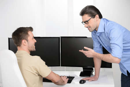 Business conversation. Two cheerful businessmen talking about business while one of them pointing computer monitorの写真素材