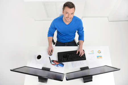Businessman at work. Top View of young cheerful businessman sitting at his working place and smiling at cameraの写真素材