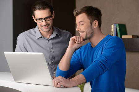 We are going up.Two cheerful businessmen dicussing something on the laptop and smilingの写真素材