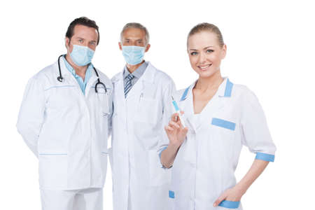Smiling beautiful nurse on foreground with syringe. Older doctors in mask on backgroundの写真素材