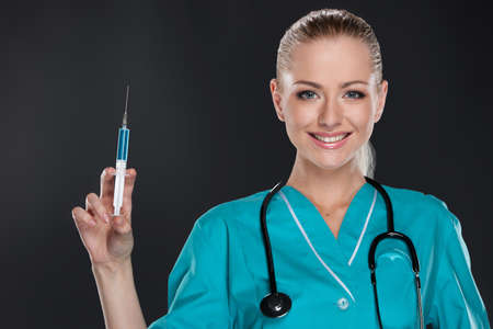 Smiling young female nurse doing injection. Isolated over black backgroundの写真素材