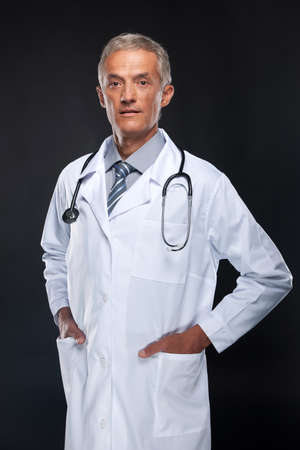 Friendly middle age doctor. Standing over black backgroundの写真素材