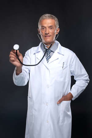 Professional doctor with stethoscope in hand. Standing isolated on black backgroundの写真素材