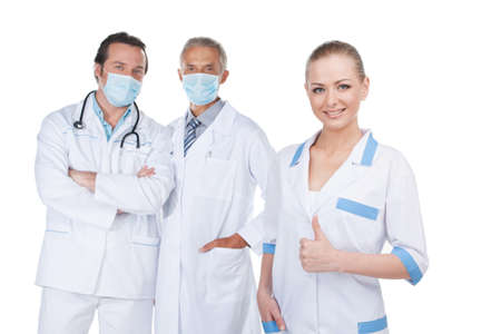Group of doctors standing together. Young nurse on foreground and two male doctors in mask on backgroundの写真素材