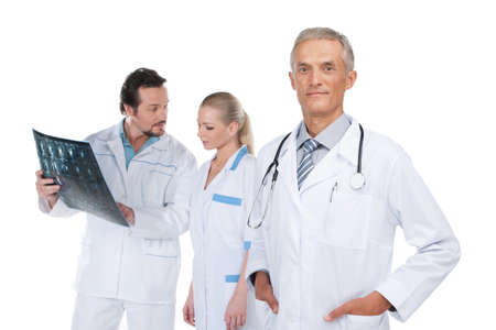 Confident and experienced Head physician on foreground. Couple of doctors discussing X-ray on backgroundの写真素材