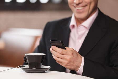 Businessman typing a message. Cropped image of businessman drinking coffee and typing a message in his mobile phoneの写真素材
