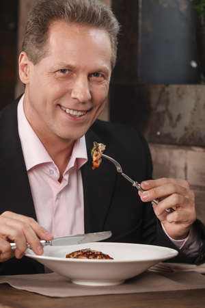Businessman in restaurant. Confident men in formal wear eating at the restaurant and smiling at cameraの写真素材