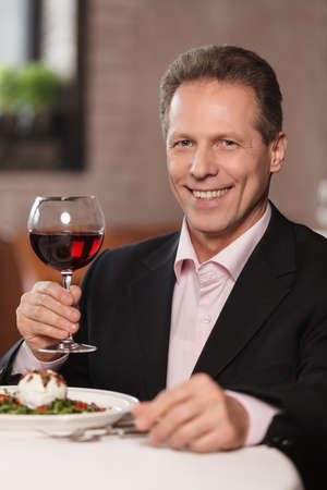 Only the best wine. Confident men in formal wear holding a glass of wine and smiling at cameraの写真素材