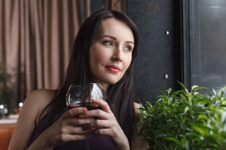 Thinking about him. Thoughtful middle-aged women standing with a glass of wine and looking awayの写真素材