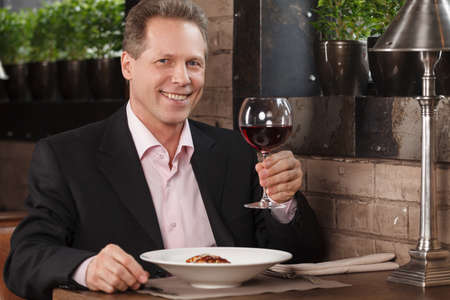 Men drinking wine. Portrait of cheerful businessman drinking wine at the restaurantの写真素材
