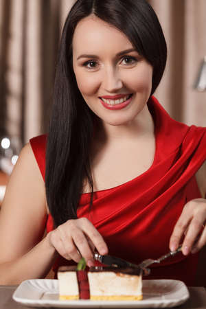 Women eating dessert. Beautiful women in red dress eating cake at the restaurantの写真素材