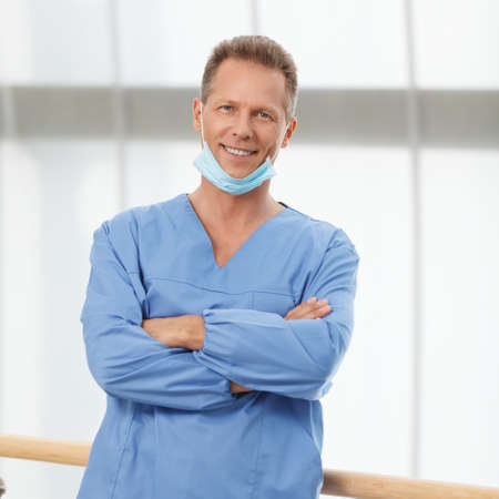 Medical expertise you can trust. Confident mature doctor in blue uniform standing with his arms crossed and smilingの写真素材