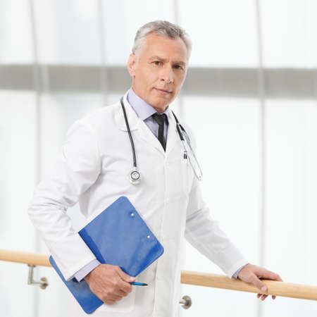 The most talented and professional doctor. Confident mature doctor standing with a clipboard and looking at cameraの写真素材