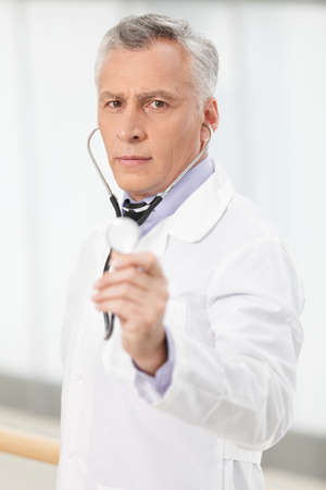 Trustworthy medical doctor. Confident mature doctor holding a stethoscope in his outstretched handの写真素材