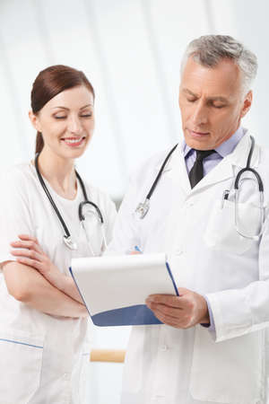 Asking for advise. Confident hospital colleagues writing in a notepad togetherの写真素材