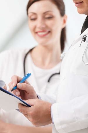 Going through a report. Close-up of two medical doctors writing in the writing pad togetherの写真素材