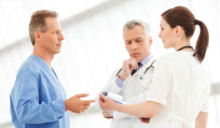 Figuring out the correct medication. Three doctors discussing the report standing close to each otherの写真素材