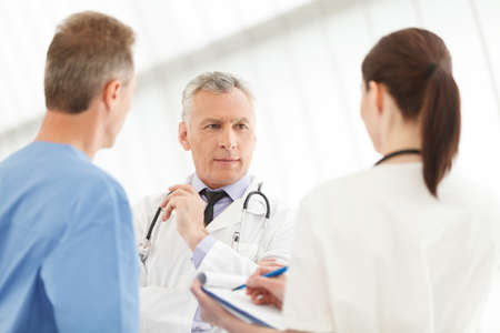 Caring team of medical healthcare professionals. Three doctors discussing the report standing close to each otherの写真素材