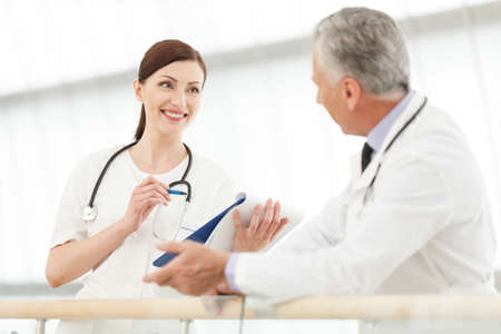 Consulting with colleague. Female doctor communicating with her colleague and writing something in the writing padの写真素材