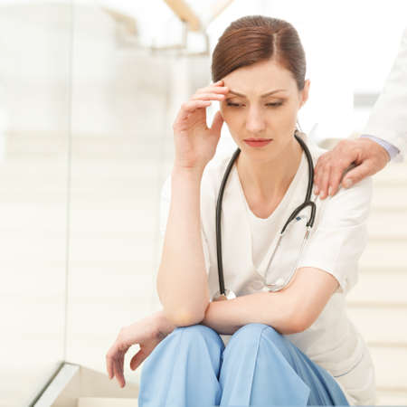 I'ts not your fault . Doctor comforting his depressed female colleague sitting on the stairs with her hand in hairの写真素材