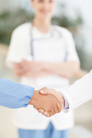 Welcome to the team. Close-up of male doctors handshaking while female doctor smiling on the backgroundの写真素材