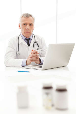 Medical doctor.Mature  doctor sitting at his working place with the medicines on the foregroundの写真素材