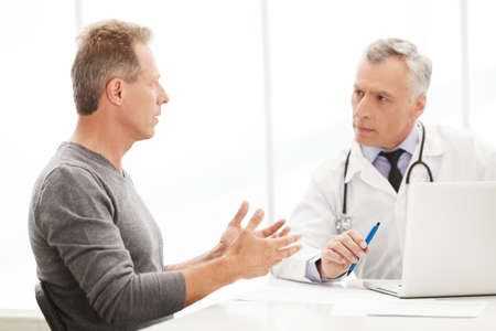 Doctor and patient. Doctor listening to the patient while he is telling about his problemsの写真素材