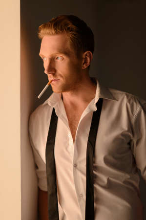 Men with cigarette. Thoughtful young men in white shirt standing with cigarette in his mouth and looking awayの写真素材
