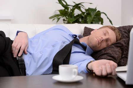 Exhausted businessman. Young tired businessman in formalwear sleeping on the couchの写真素材