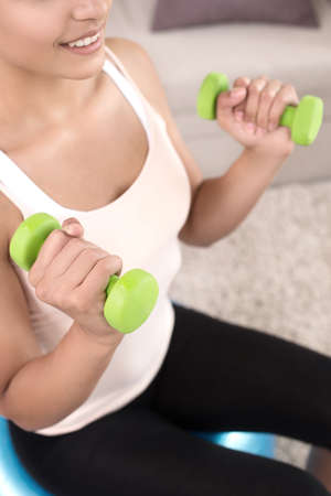 Sports at home. Top view of beautiful young women exercising at home while sitting on the fitness ball and using the dumbbellsの写真素材