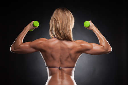 Back of beautiful sexy bodybuilder woman with green dumbbells. Standing isolated over black backgroundの写真素材