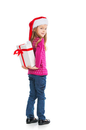 Small blond girl hiding big present behind back. Looking at camera over shoulder smiling isolated on white backgroundの写真素材
