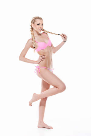 Sexy young blond girl fashion posing in pink bikini. Showing beautiful legs isolated over white backgroundの写真素材