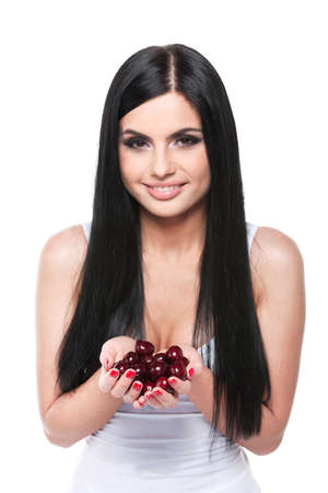 Portrait of Beautiful brunet young woman in white shirt. Holding a handful of red cherries isolated over white backgroundの写真素材